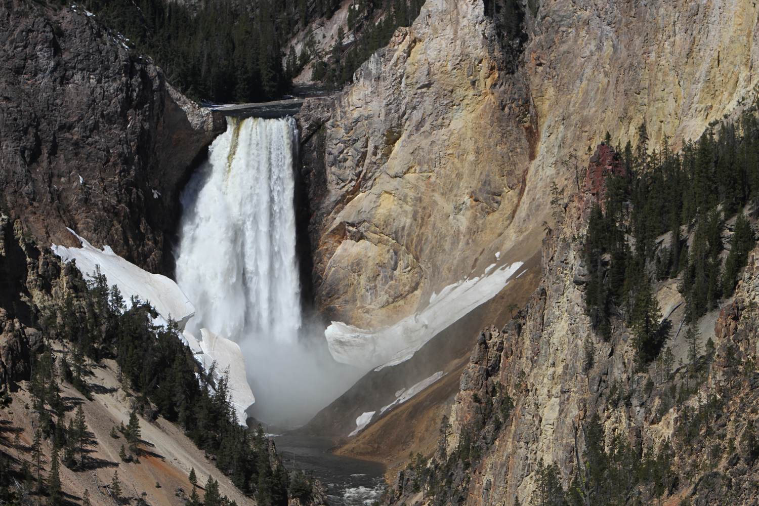 The Lower Falls of the Yellowstone dropping into the canyon between snow patched rock.